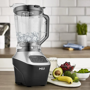 Blender on a kitchen counter with fruits and vegetables, featuring the brand 'MIUI'.